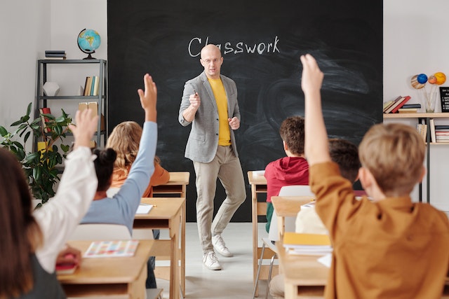 a teacher standing in front of a class as students raise their hands